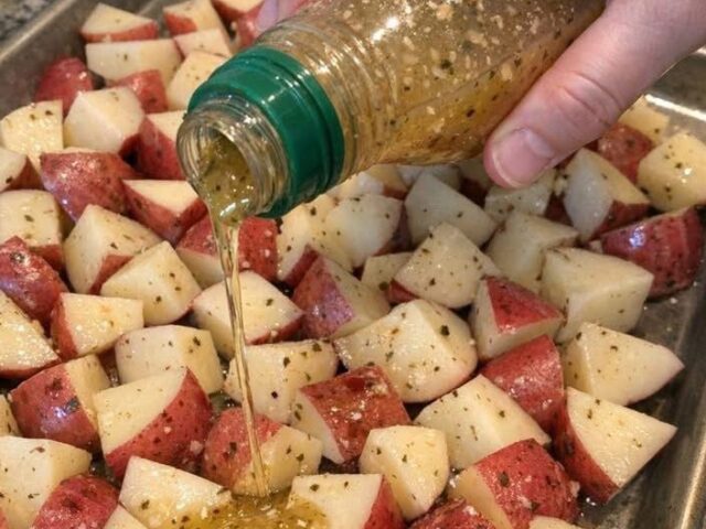 Cubed red potatoes on a sheet pan with Italian dressing being poured over them